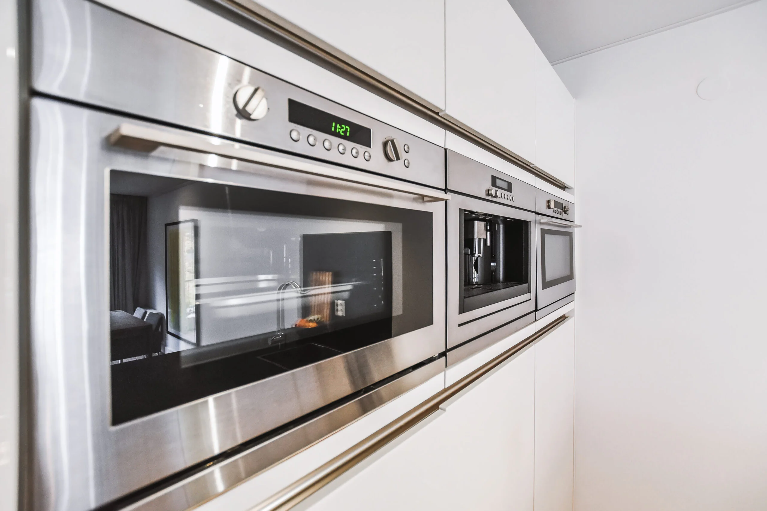 Stainless steel oven, microwave, and coffee maker professionally installed in a modern kitchen.